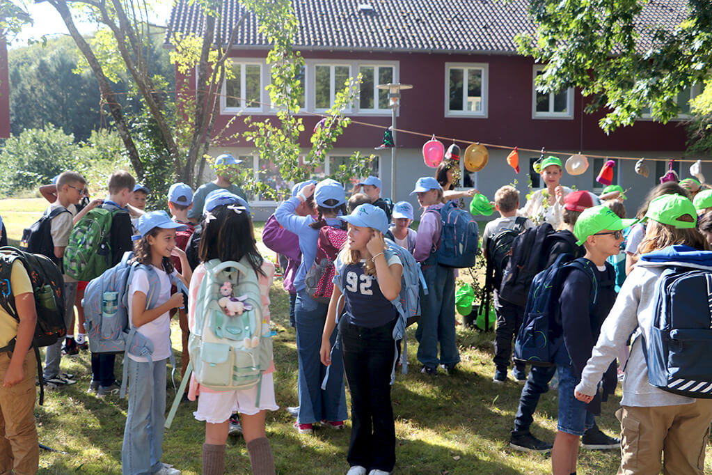 Eine Gruppe von Kindern mit Rucksäcken und Mützen versammelt sich draußen vor einem Gebäude und bunten Dekorationen.