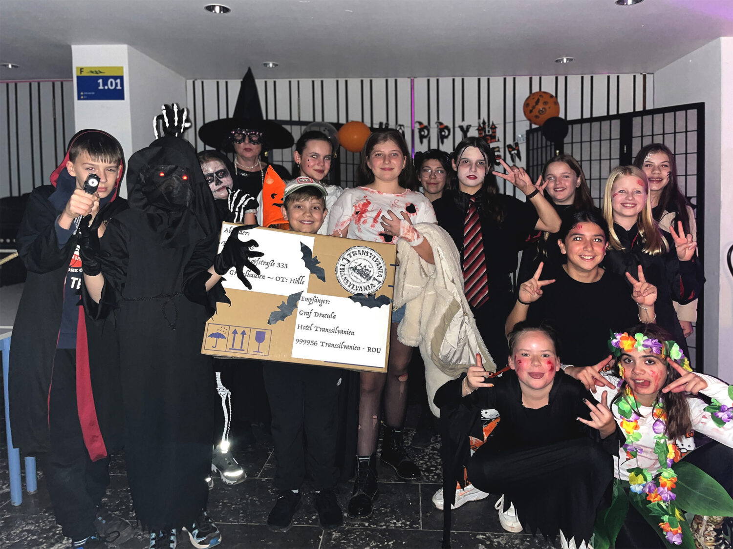 Eine Gruppe von Kindern in Halloween-Kostümen, die auf einer Party zusammen posieren, einige halten Requisiten und machen Friedenszeichen.