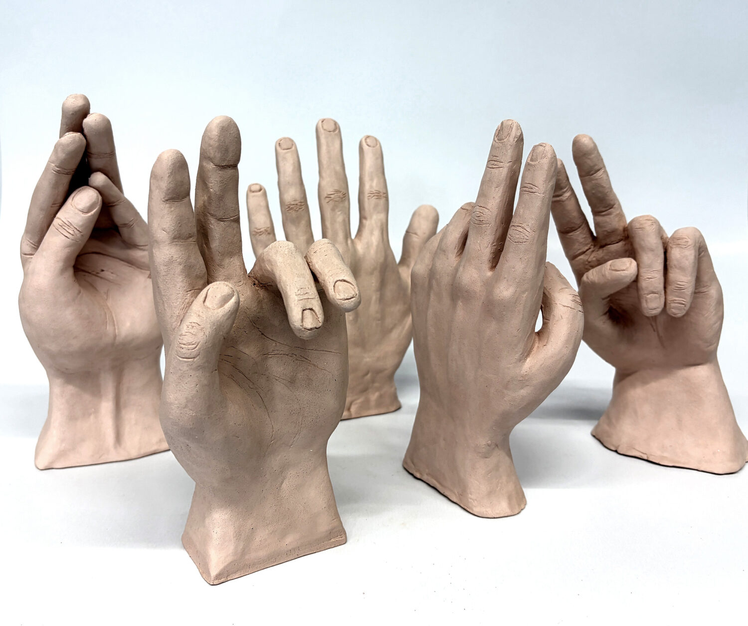 Fünf realistische Tonskulpturen von Händen mit verschiedenen Gesten auf einem schlichten weißen Hintergrund.