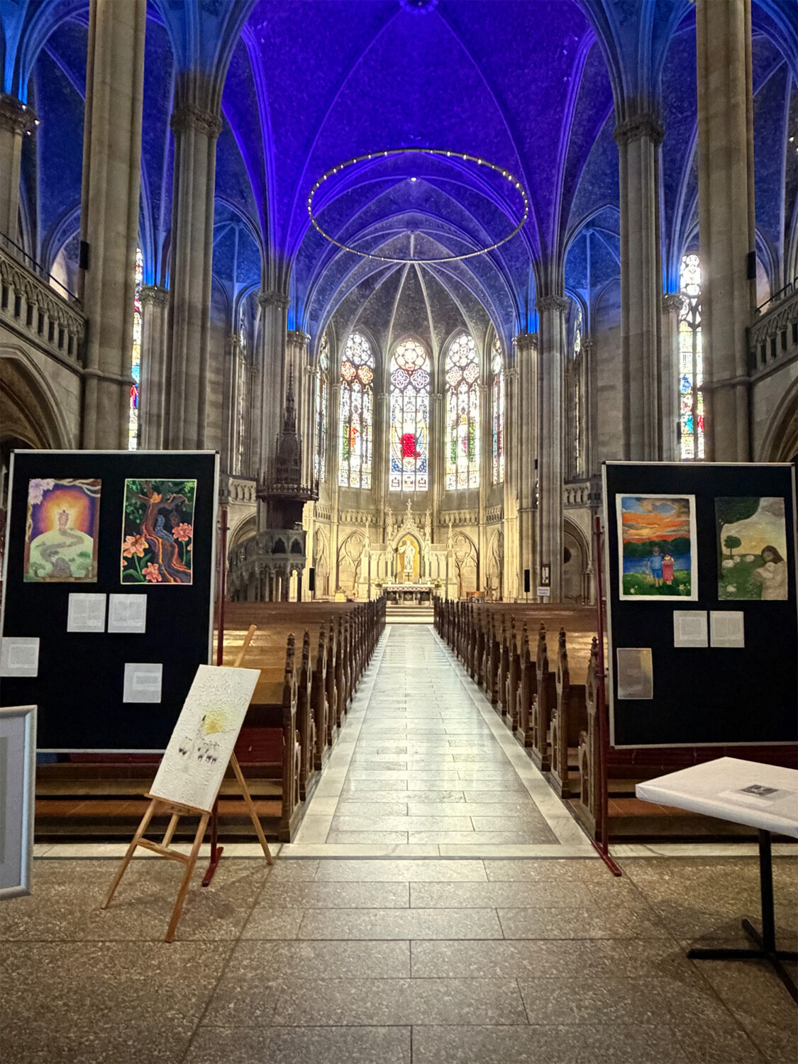 Kathedraler Innenraum mit hohem Gewölbe, Glasmalerei und Kunstausstellungen am Eingang der Kirchenbänke.